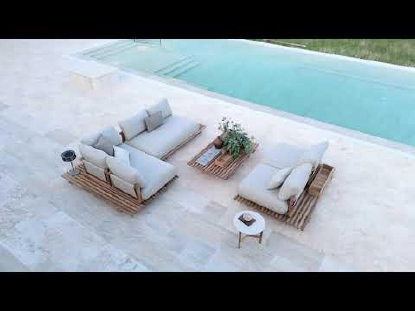 Sitzbereich im Freien neben dem Pool mit zwei gepolsterten Sofas und einem niedrigen Tisch auf einer hellen Steinterrasse, dekoriert mit Topfpflanzen und einem kleinen runden Beistelltisch.