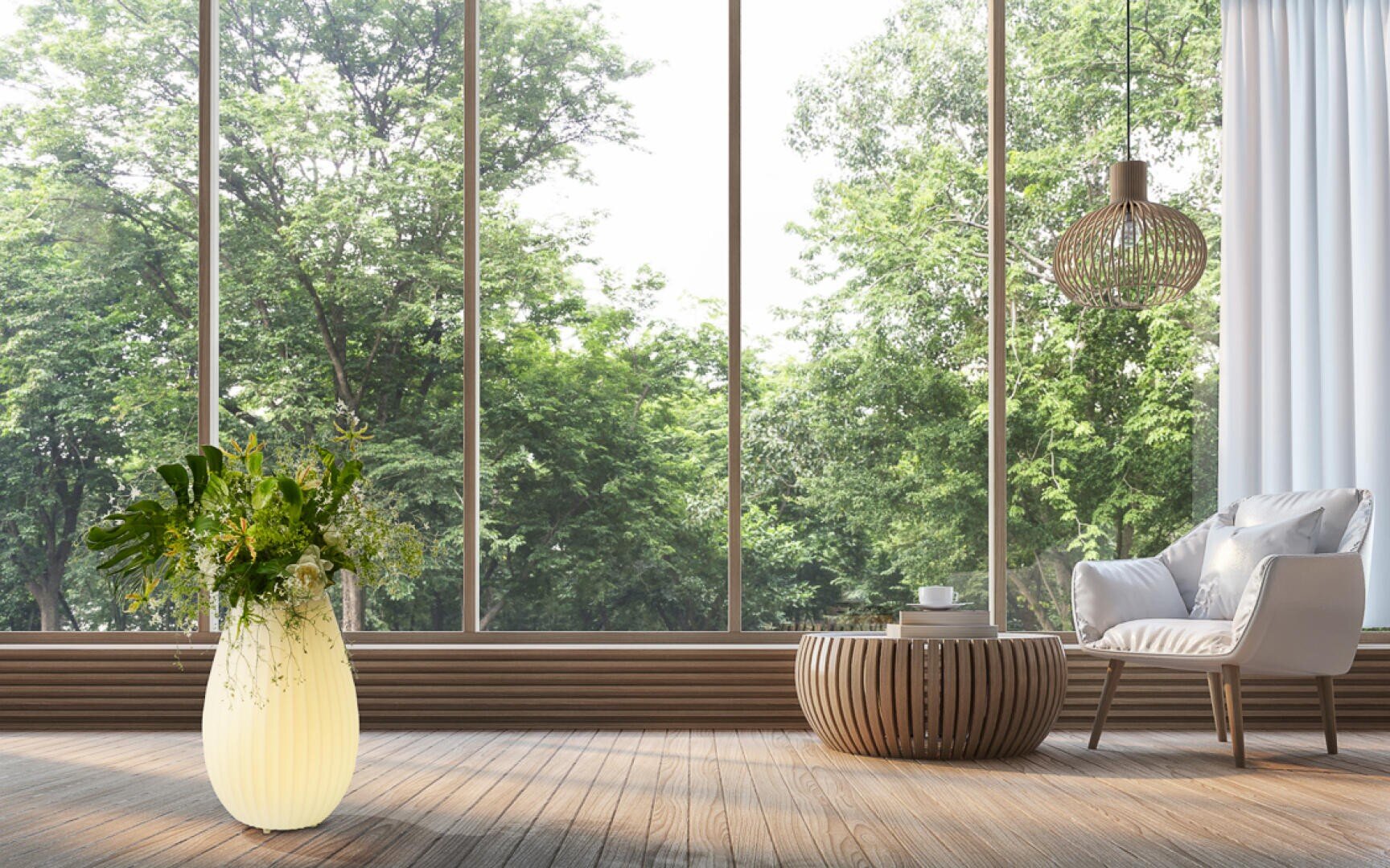 Ein helles, modernes Wohnzimmer mit großen Fenstern und Blick auf grüne Bäume, mit einem weißen Sessel, einem runden Couchtisch aus Holz, einer Hängelampe und einer leuchtenden Vase mit Blumen auf einem Holzboden.