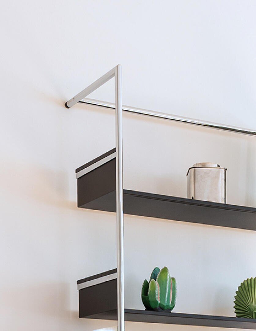 Nahaufnahme eines modernen Wandregals mit Metallrahmen, das einen kleinen Kaktus, ein grünes Dekorationsobjekt und einen Marmorbehälter vor einer weißen Wand hält.