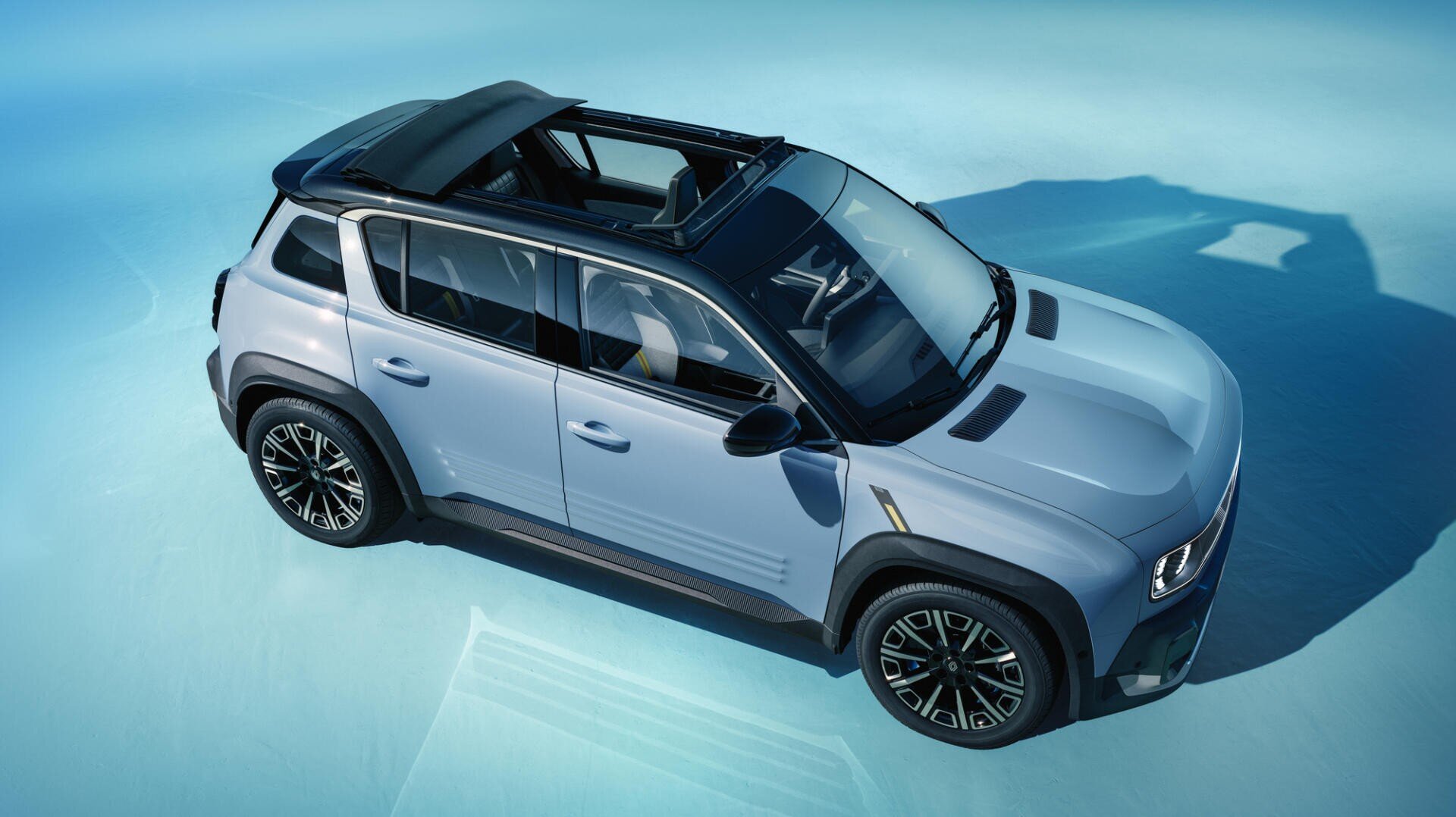 A light blue SUV with a panoramic roof and black trim, viewed from above and at an angle, parked on a smooth, blue-lit surface. The sunroof is partially open and provides a view of the interior seats.