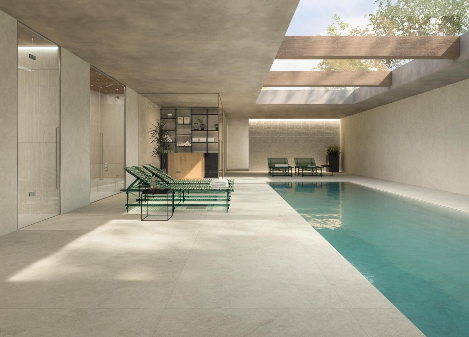 Ein moderner Innenpool mit hellem Steinfliesenboden, zwei grünen Liegestühlen, großen Oberlichtern und einfallendem Sonnenlicht. Am anderen Ende, in der Nähe eines gläsernen Raums, stehen Topfpflanzen und weitere Liegestühle.