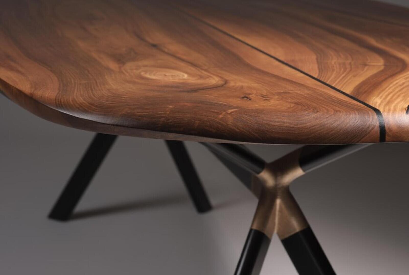 Close-up of a wooden table with a smooth, polished surface and natural wood grain, supported by black metal legs with a unique joint design.