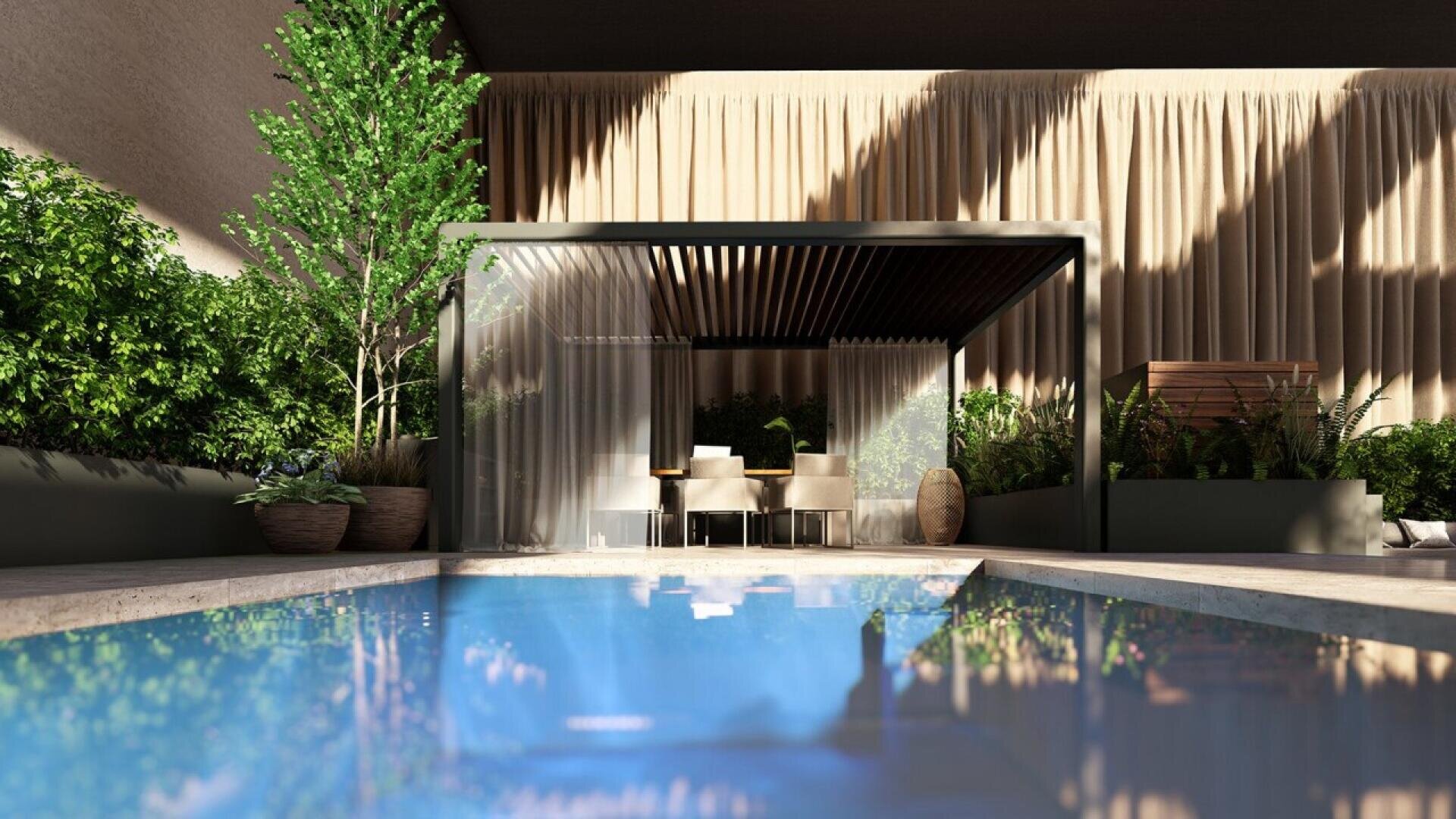 Modern outdoor area with a pool in the foreground, greenery along the sides, and a shaded seating area with a dining table and chairs, backed by large beige curtains. Sunlight creates reflections on the water.