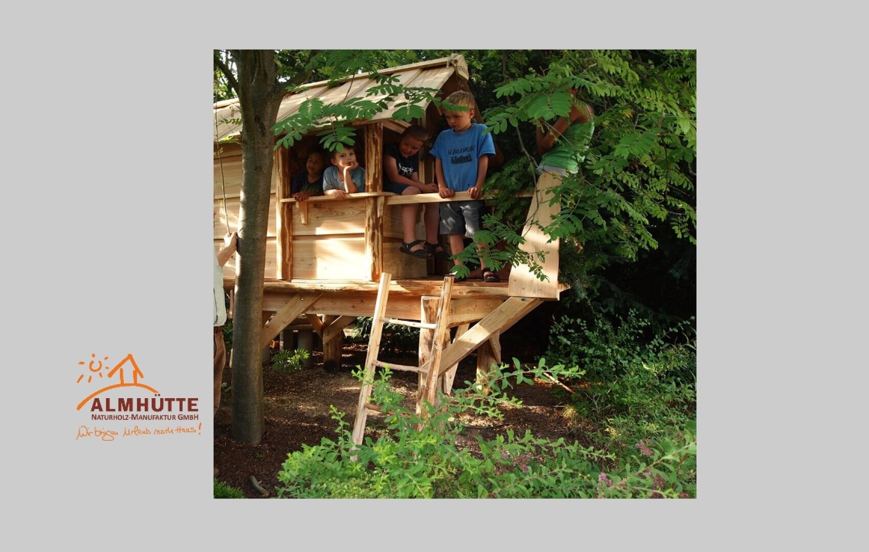 Several children stand and lean over the railing of a wooden tree house surrounded by lush green trees. Sunlight filters through the leaves and a logo of the mountain hut appears in the bottom left corner.