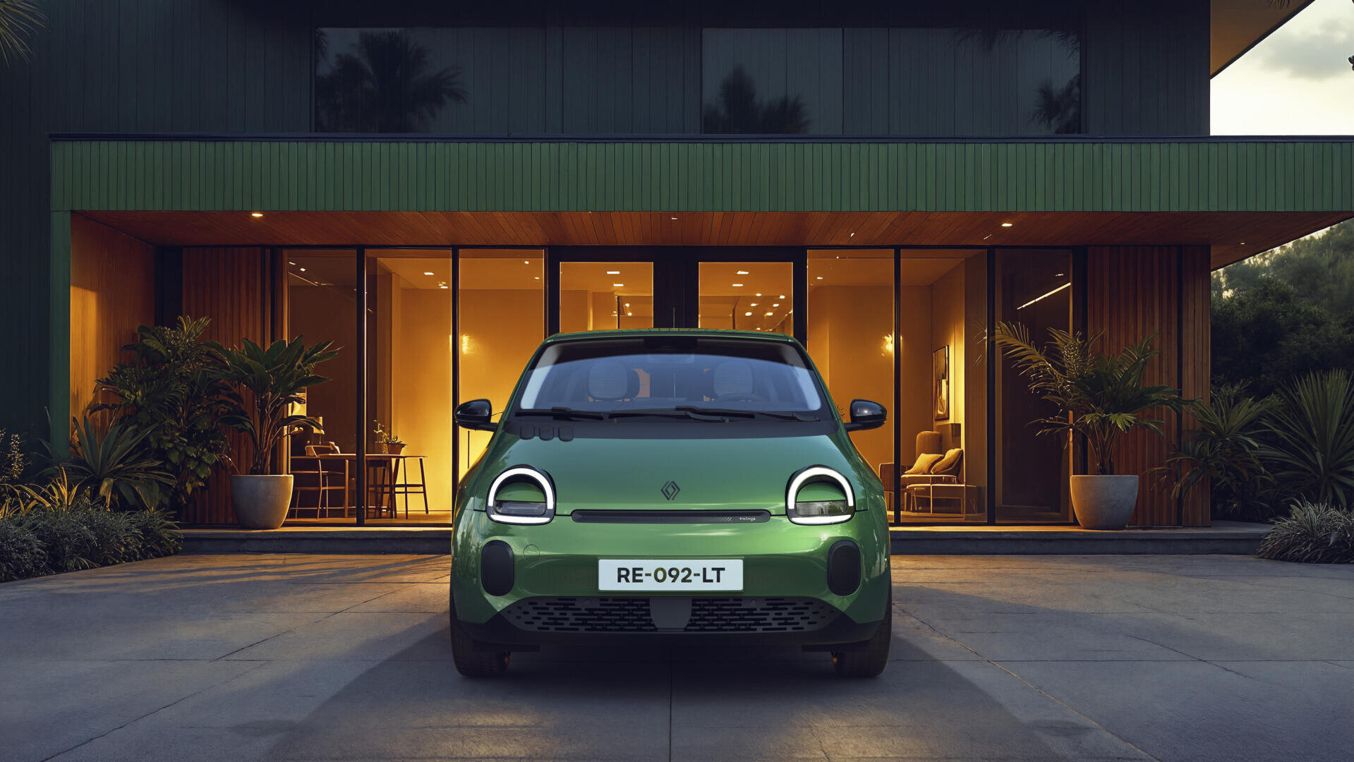 Ein kleines grünes Elektroauto parkt vor einem modernen Haus mit großen Glasfenstern, warmer Innenbeleuchtung und tropischen Pflanzen auf beiden Seiten des Eingangs.