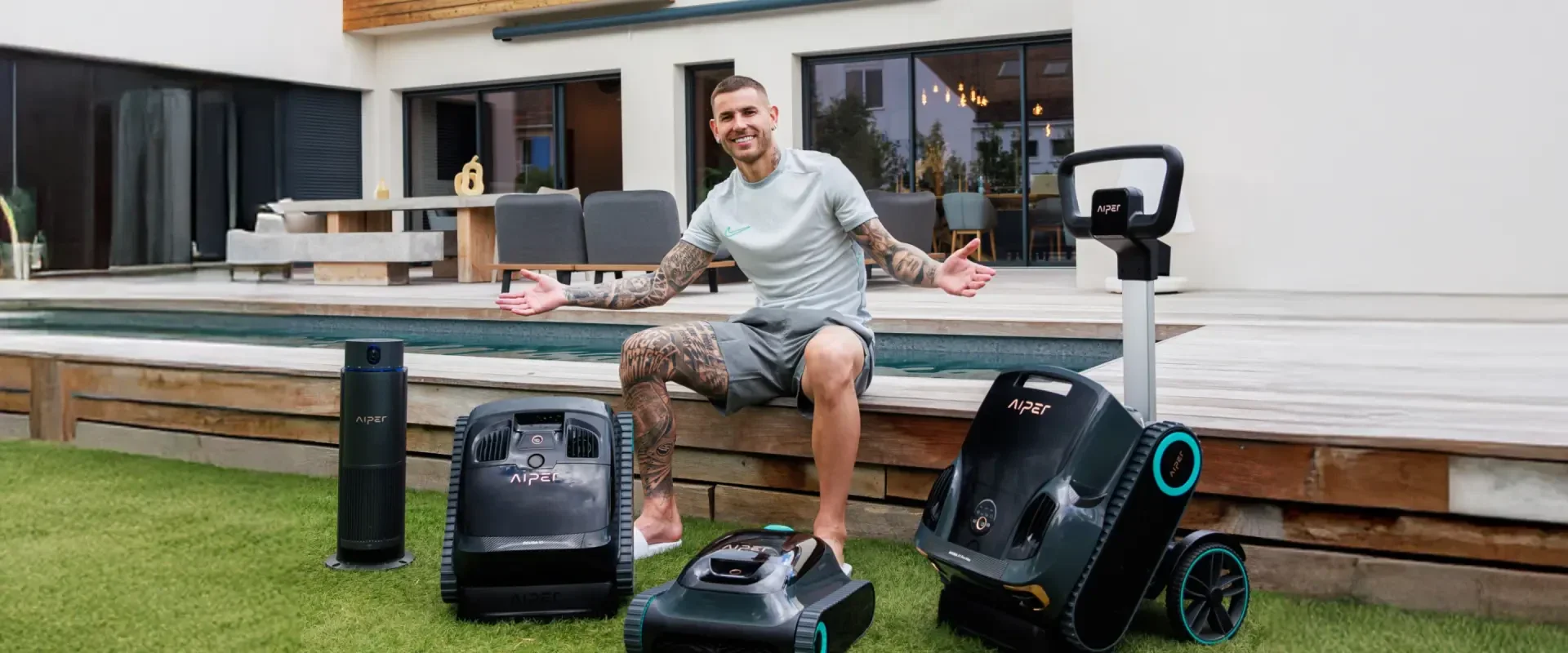 A man with tattoos sits by a modern pool with a lawn, smiling with his arms outstretched, surrounded by four high-tech robots on the lawn, in front of a modern house with large windows and outdoor seating.