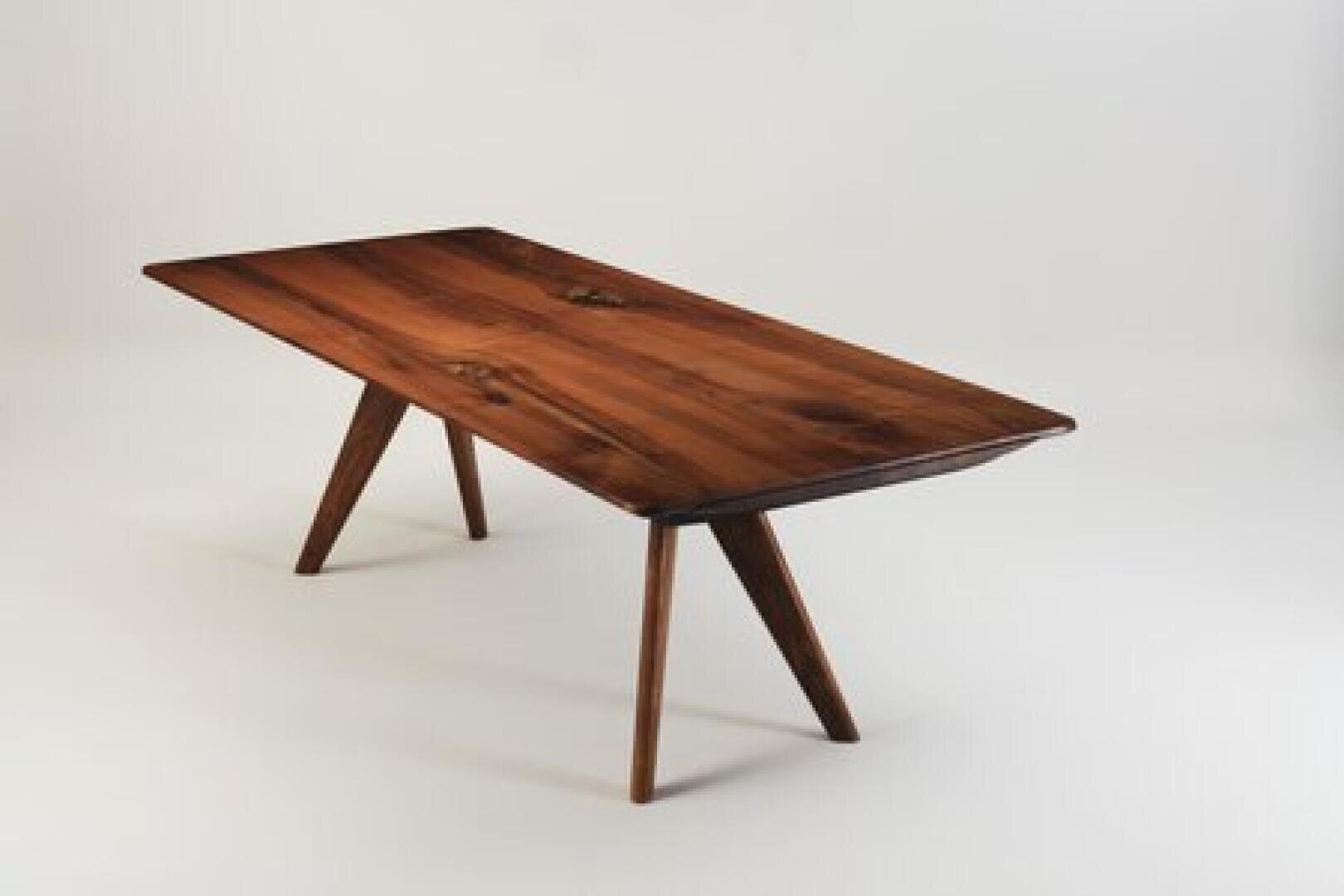 A rectangular wooden table with angled legs, featuring a smooth, dark wood grain surface, set against a plain white background.