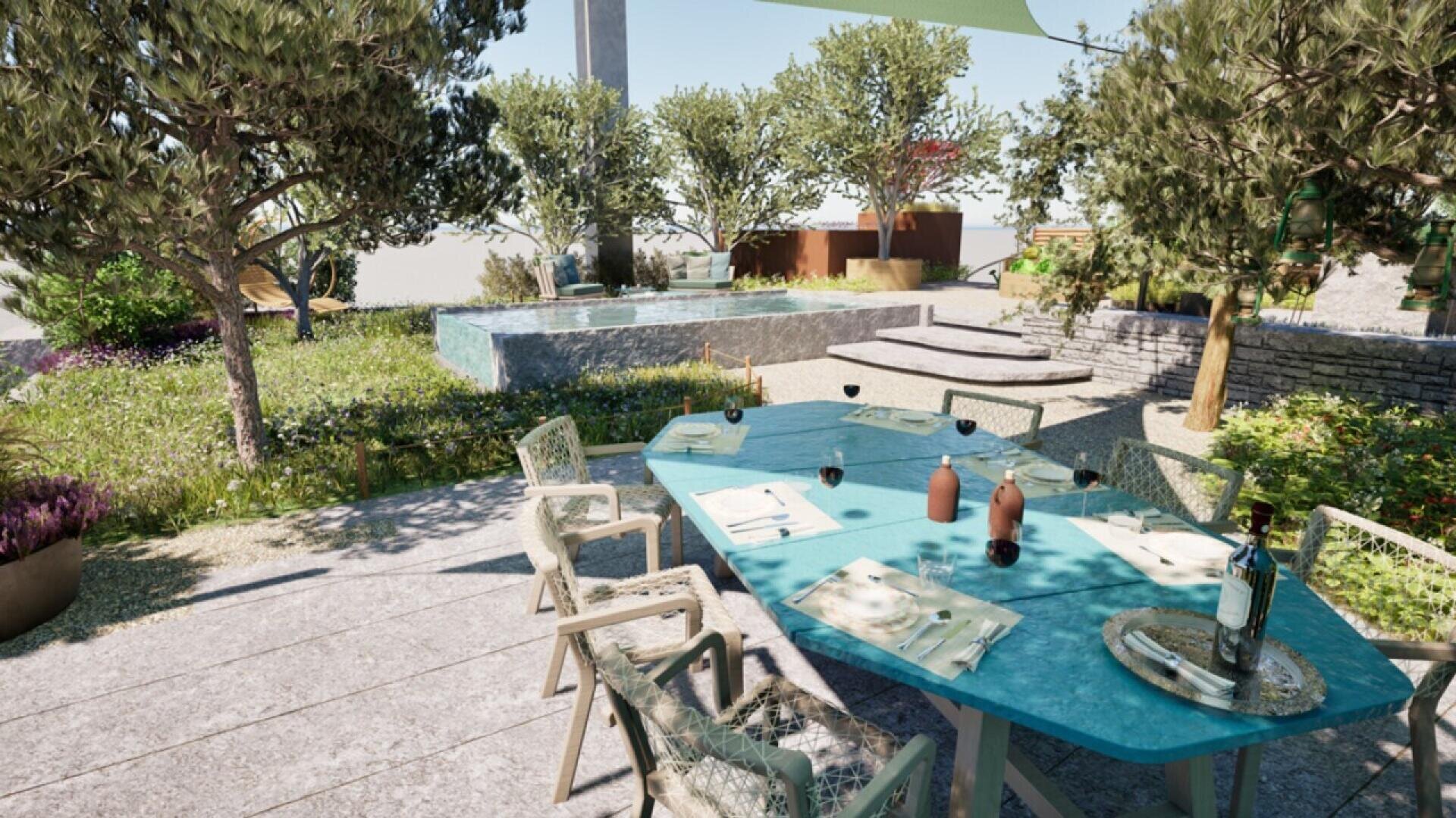 Outdoor dining area with a turquoise table set for six on a stone patio, surrounded by green trees and plants. In the background, there is a small pool and stone steps leading up to a grassy garden.