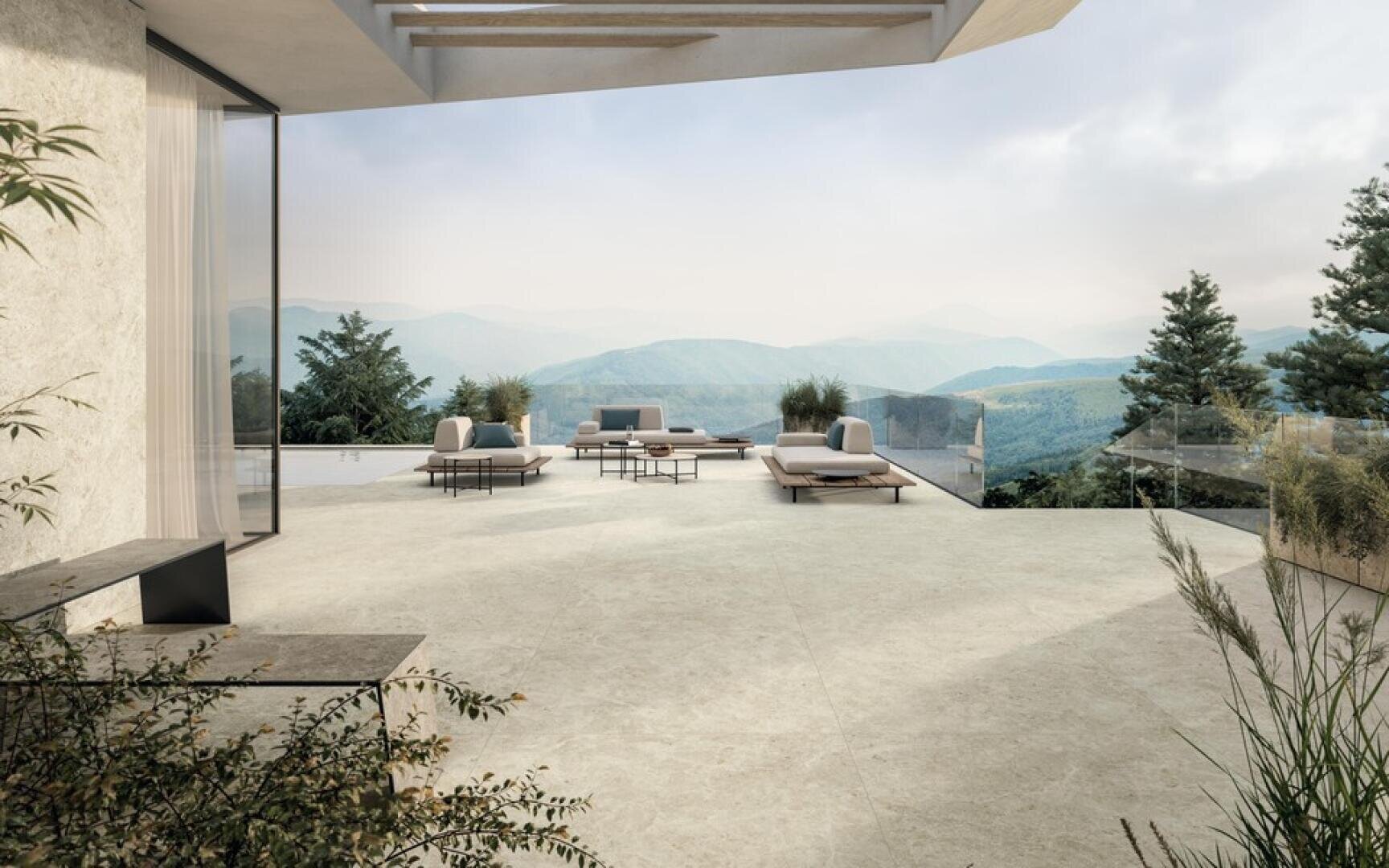 Moderne Außenterrasse mit minimalistischen Loungesesseln und Tischen mit Blick auf malerische grüne Berge und Täler unter einem bewölkten Himmel. Glasakzente und helle Steinfliesen schaffen eine ruhige, offene Atmosphäre.