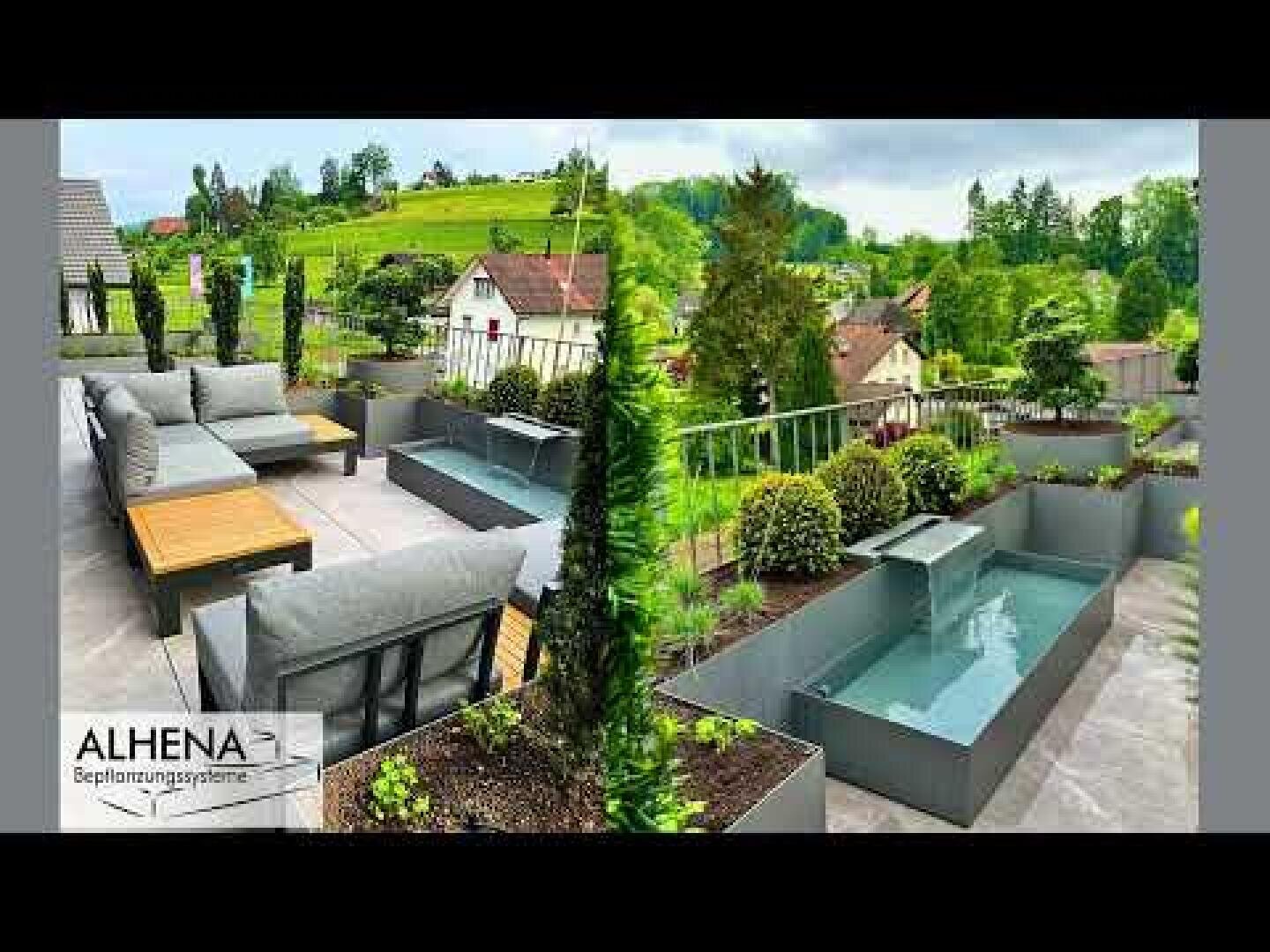 Moderne Dachterrasse mit grauen Sofas, Holztischen, Pflanzgefäßen mit hohen Grünpflanzen und einem kleinen rechteckigen Wasserspiel mit Blick auf eine malerische, grüne Wohngegend. Alhena-Logo in der unteren linken Ecke.