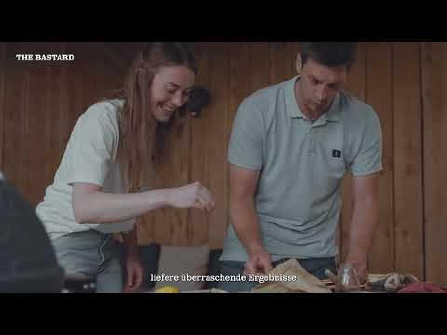 A woman and a man stand smiling at a wooden table and prepare food together in an interior. The text on the picture reads THE BASTARD and delivers surprising results.