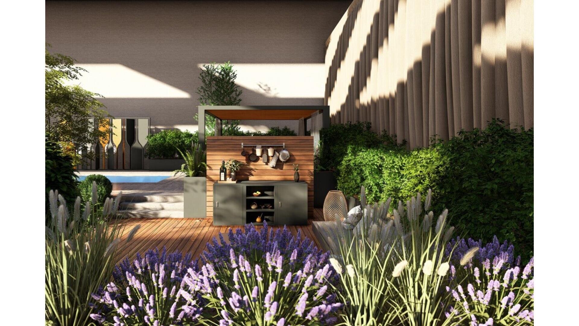 A modern outdoor patio with a wooden deck, lush green plants, purple flowers in the foreground, a small pool, and a shaded kitchen area with shelves and utensils. Sunlight casts shadows on the wall and floor.