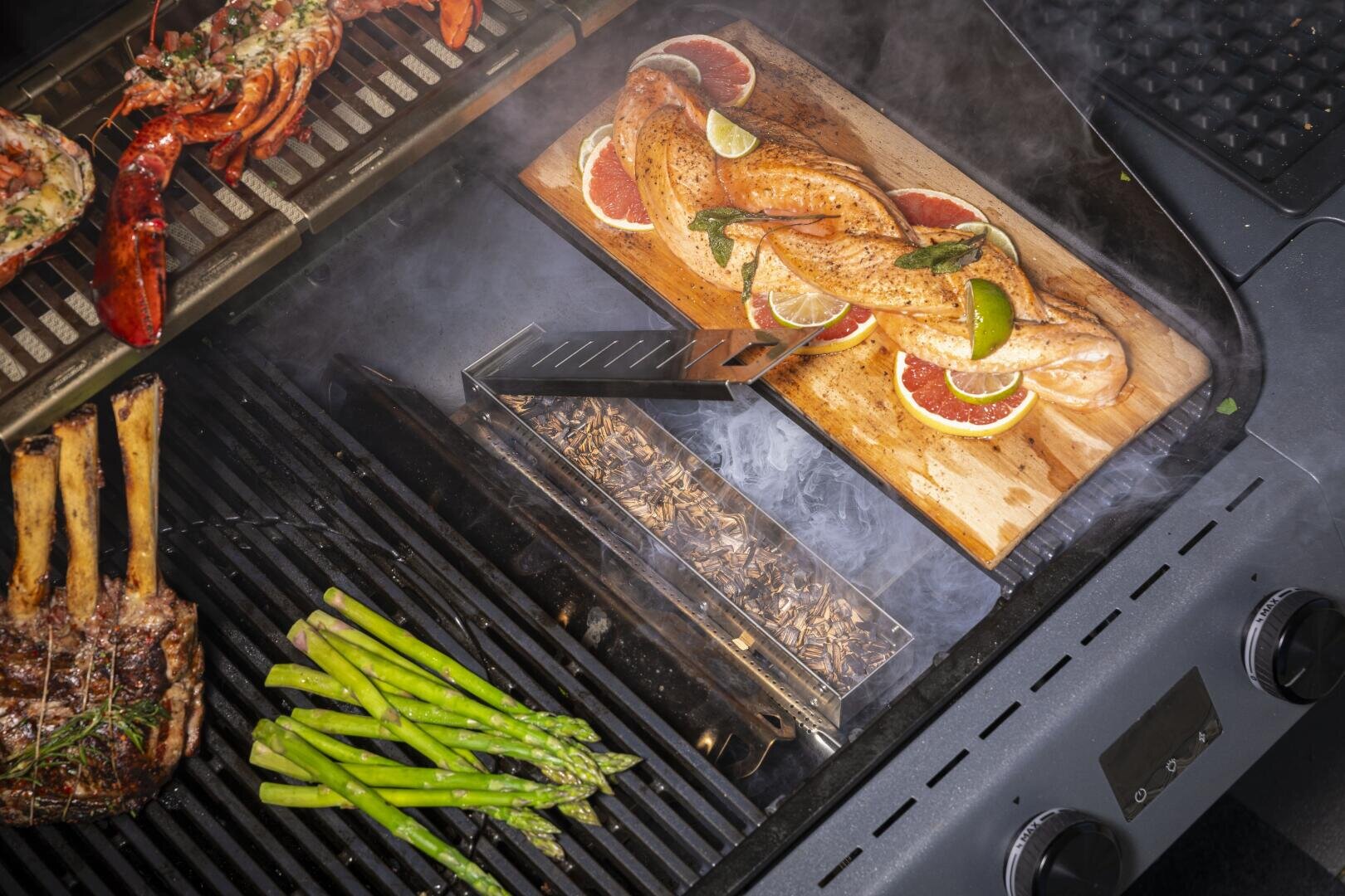 Grill smoked salmon on a cedar plank with lime and herbs, lobster tails, asparagus and a rack of lamb; a smoker box with wood chips provides additional flavor.