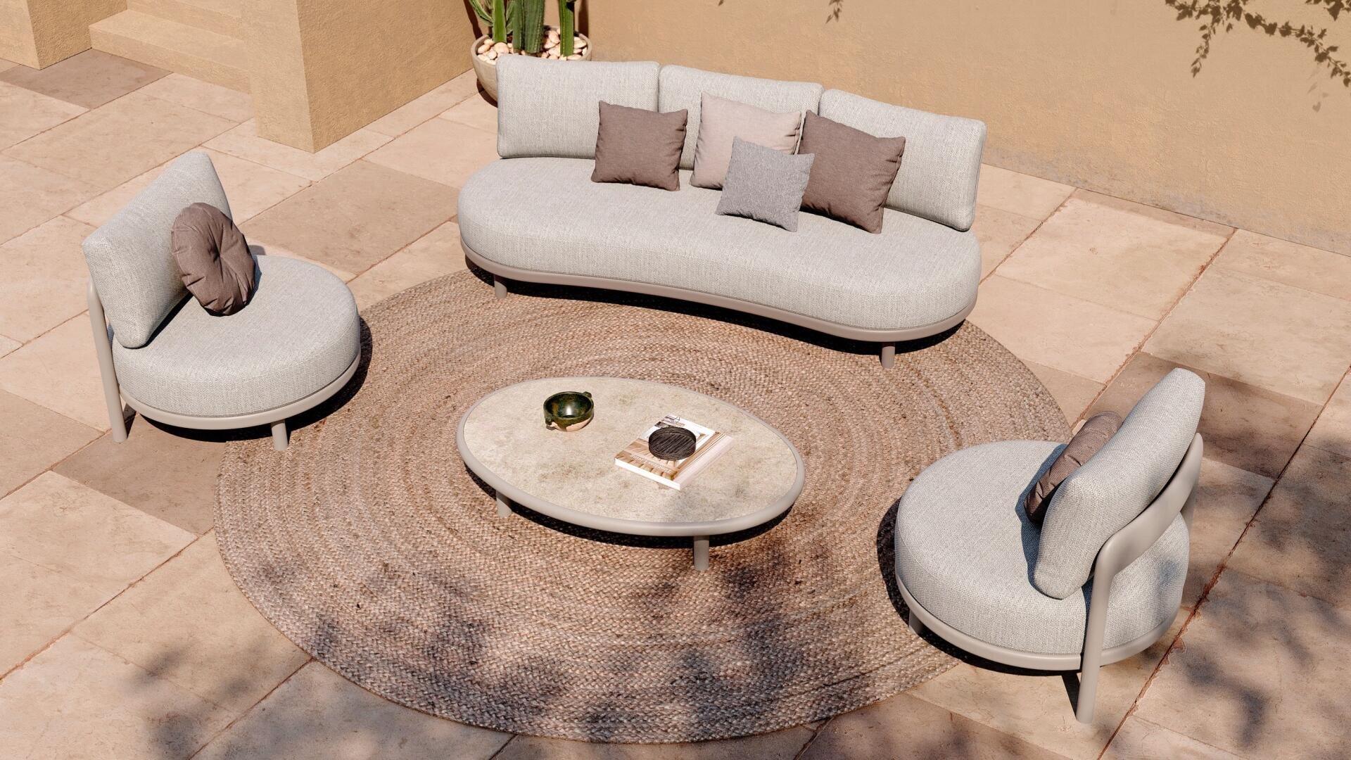 Ein geschwungenes hellgraues Sofa, zwei passende Stühle und neutrale Kissen umgeben einen ovalen Couchtisch auf einem runden Webteppich in einem Terrassenbereich mit beigen Fliesen und Topfpflanzen im Hintergrund.