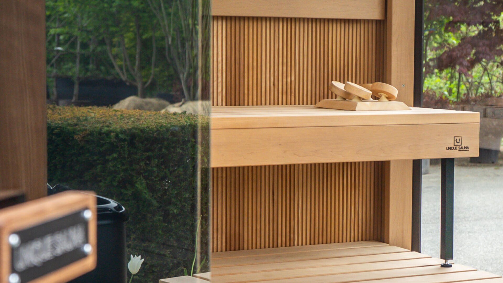 Ein hölzernes Regal mit zwei kleinen hölzernen Flugzeugen auf der Oberseite, die an vertikalen Holzlatten angebracht sind. Die Spiegelungen im Glas zeigen grüne Büsche und Bäume draußen.