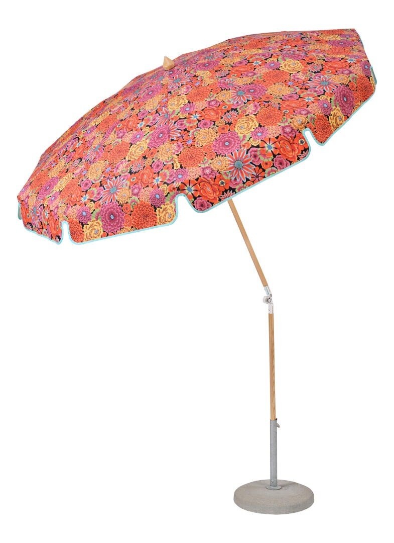 Ein großer Sonnenschirm für den Außenbereich mit einer Holzstange und einem farbenfrohen, blumengemusterten Stoffdach in Rot-, Orange- und Rosatönen auf einem runden grauen Sockel.