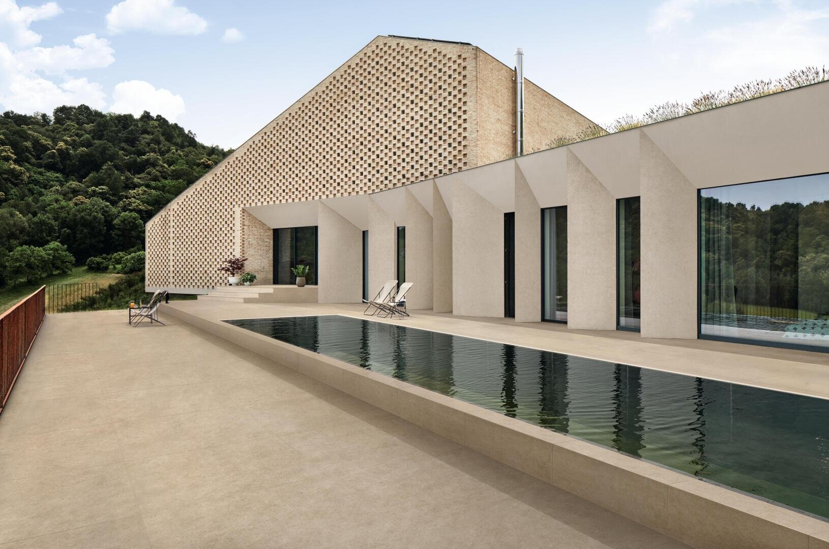 Ein modernes Haus mit geometrischer Architektur, großen Fenstern, einer einzigartigen Lochziegelfassade und einem langen, schmalen Außenpool auf einer großen Terrasse, umgeben von Grün und bewaldeten Hügeln.