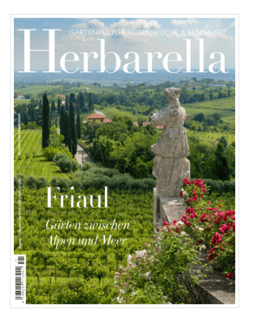 Cover of Herbarella magazine featuring a scenic view of lush green vineyards, cypress trees, and rolling hills in Friuli, Italy, with a stone statue and pink flowers in the foreground.