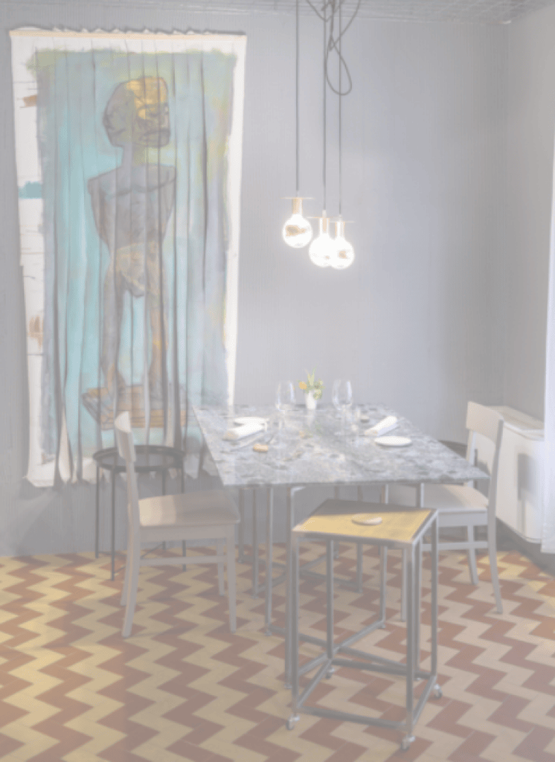 Ein kleiner Essbereich mit einem Marmortisch für vier Personen, umgeben von Stühlen. Darüber hängt ein Trio von leuchtenden Pendelleuchten. An der Wand hängt ein großes abstraktes Gemälde mit einer stehenden Figur. Der Fußboden hat ein rot-cremefarbenes Chevron-Muster.
