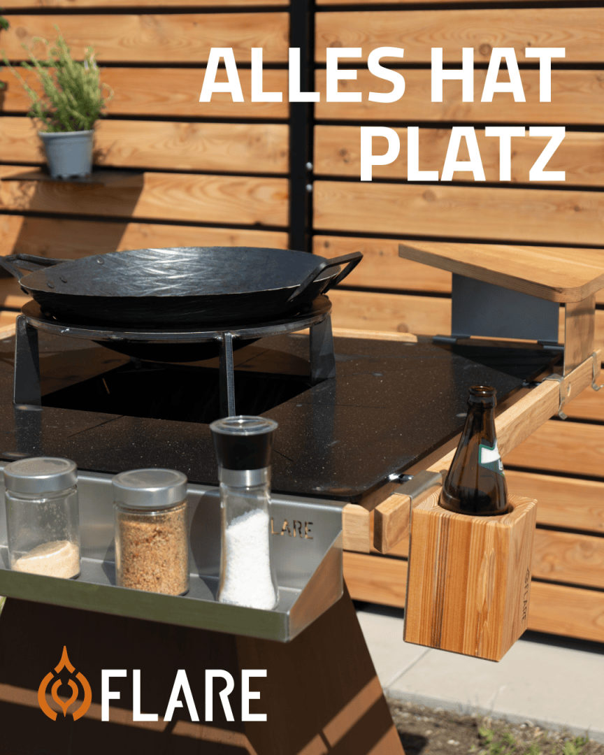 A modern outdoor barbecue station with a large black pan, spice jars, a beer bottle in a wooden holder and the text EVERYTHING HAS PLACE and FLARE above and below. Wooden fence in the background.