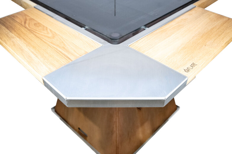 Close-up of a modern table with a metal and light wood surface, featuring a geometric pattern and a square central area. The edge is engraved with a brand that reads "FLARE".