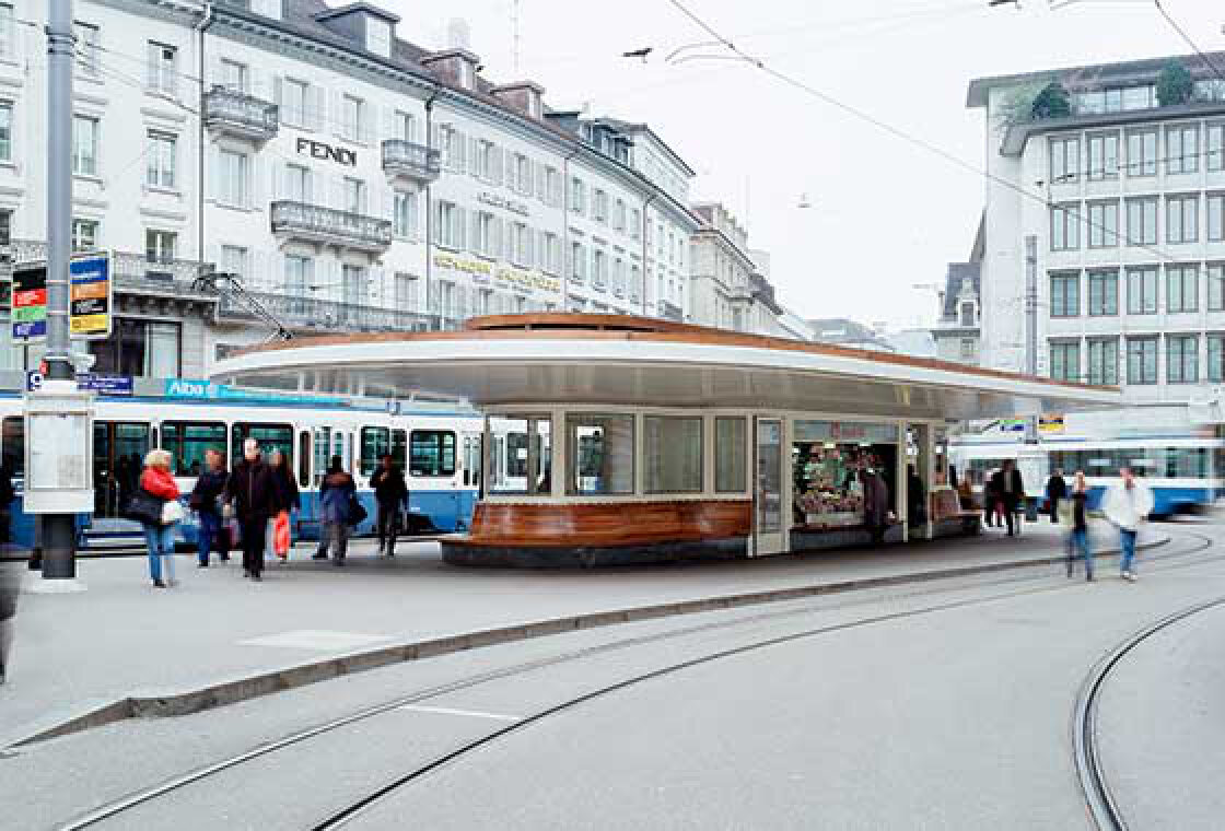 A modern tram station with a curved roof and a wooden bench, surrounded by people walking and waiting. Blue and white trams are visible, with historic buildings and shops in the background.