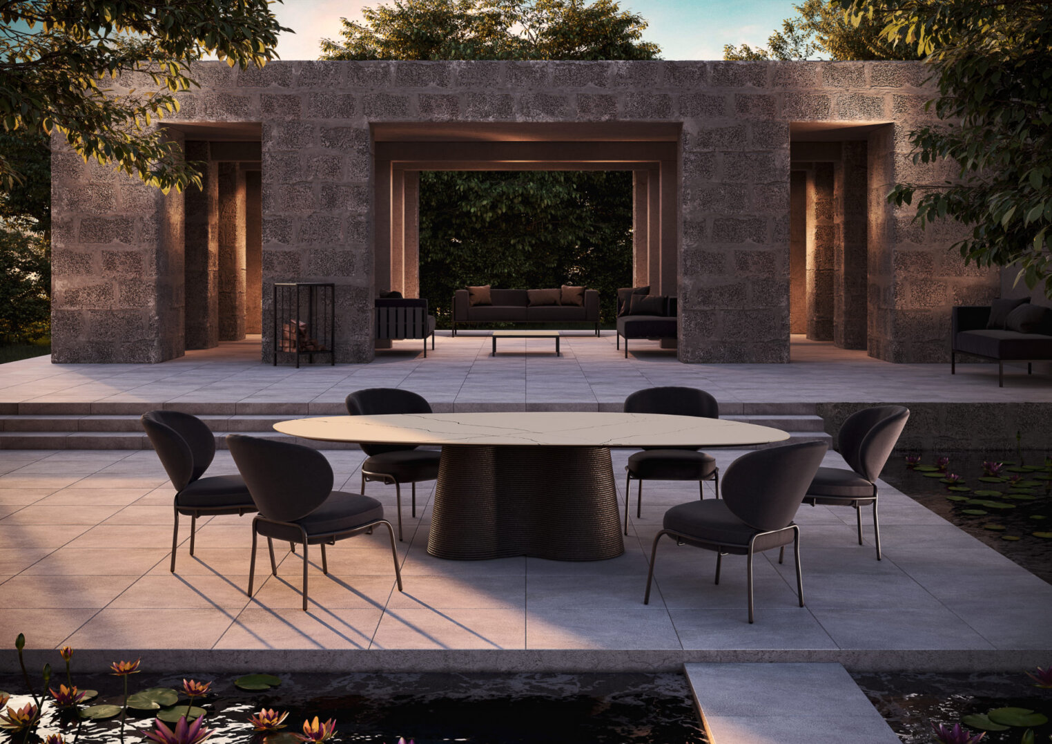 A modern outdoor dining area consists of a round table with black chairs set on a tiled terrace near a pond with lily pads. In the background is a stone structure with seating, surrounded by trees and greenery.